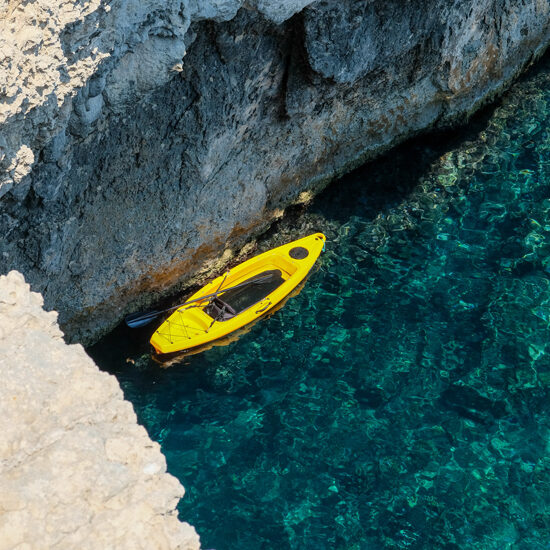 yellow kayak stopped against a cliff in transparent water