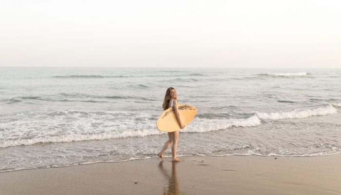 chica-sosteniendo-tabla-surf-pie-cerca-orilla-mar