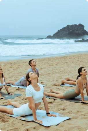 Group yoga session on a beach during sunset.